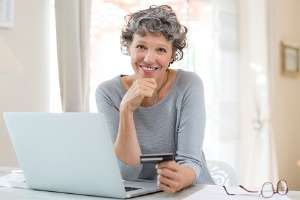 Adult woman sitting at computer with credit card in hand.